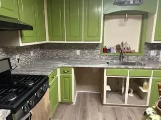 A kitchen with green cabinets , a stove and a sink.