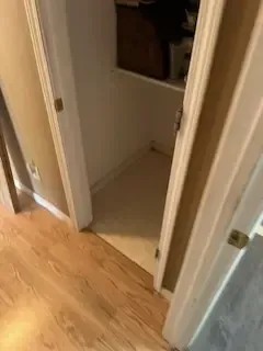 A hallway with hardwood floors and a closet with a door open.