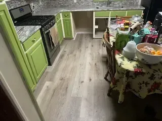 A kitchen with green cabinets , a stove , a table and chairs.