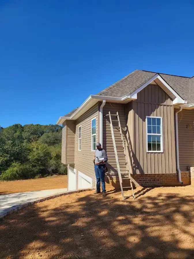 A man is standing in front of a house with a ladder.