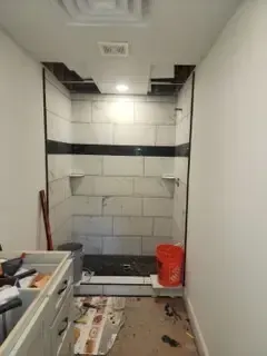 A bathroom with a shower and a bucket on the floor.