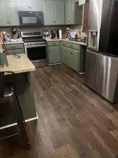 A kitchen with green cabinets , stainless steel appliances , a refrigerator and a microwave.