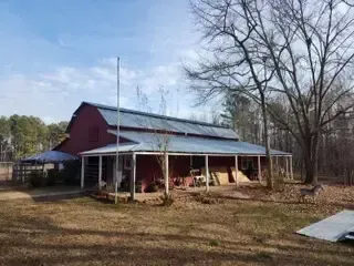 A red barn with a metal roof and a porch in the middle of a field.