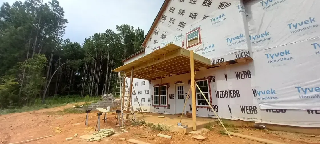A house is being built with a porch and trees in the background.
