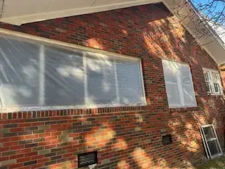 A brick house with a lot of windows covered in plastic.