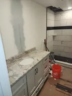A bathroom with a sink , cabinets , and a red bucket.