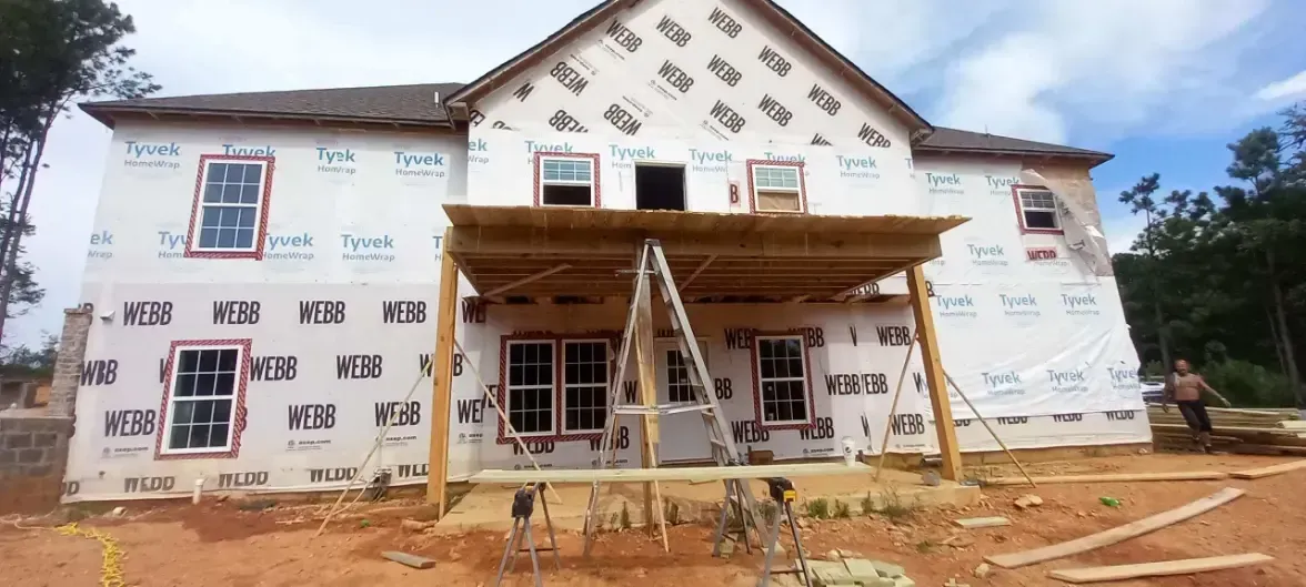 A large house is being built in the middle of a dirt field.