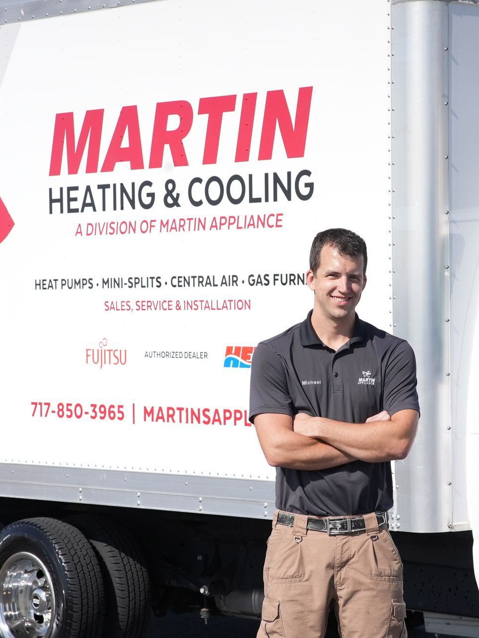 A man is standing in front of a martin heating and cooling truck.