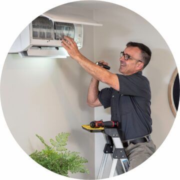 A man is standing on a ladder fixing an air conditioner.