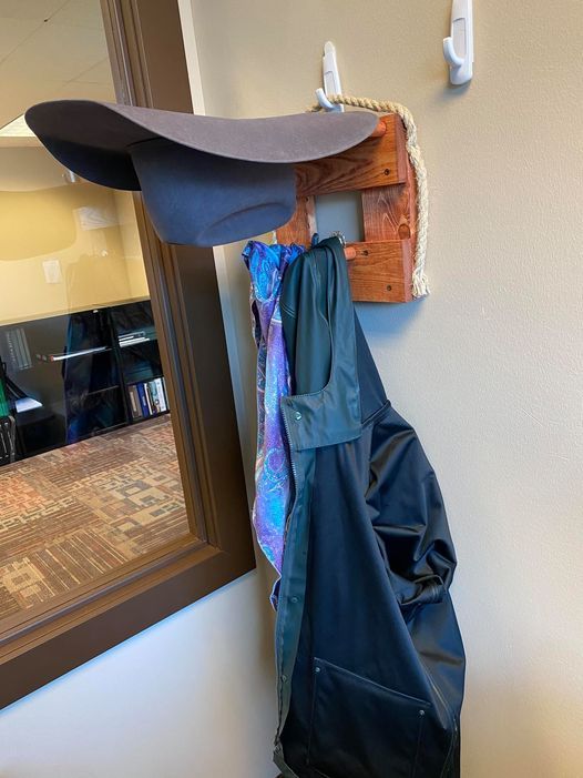 Hat and coat hanging on a wooden wall rack, near a mirror.