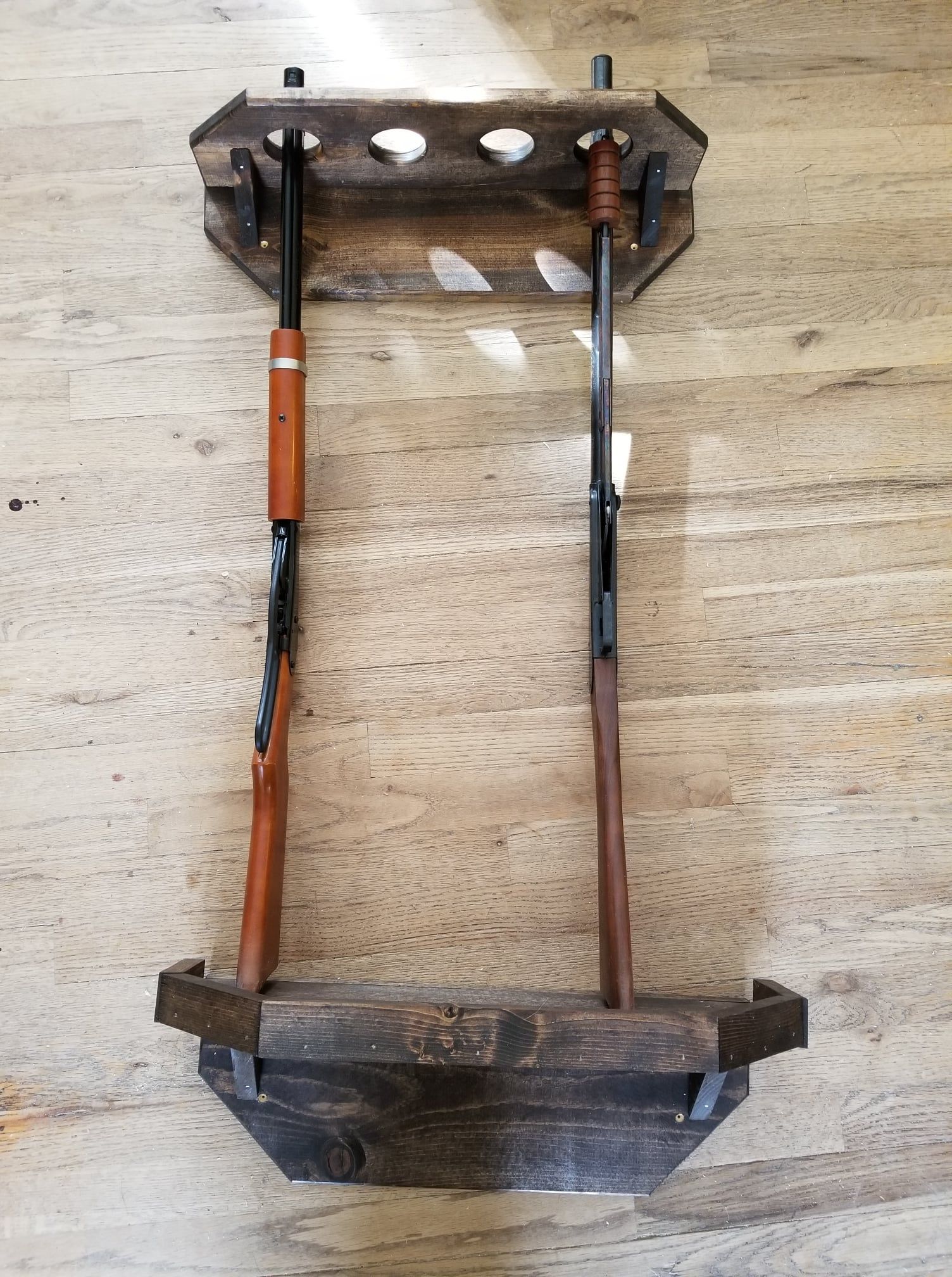 Wooden gun rack holding two rifles on a wood-paneled wall.