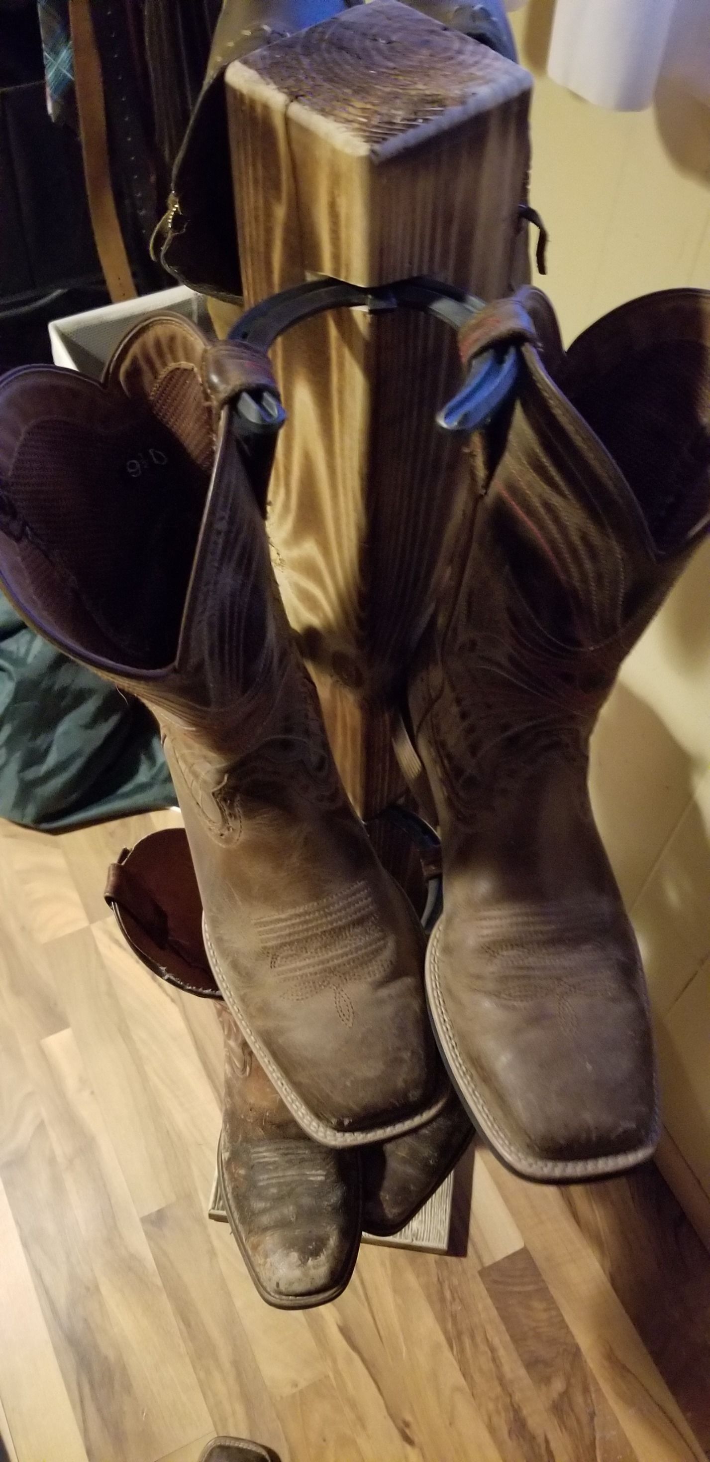 Pair of brown cowboy boots hanging on a wooden boot stand.