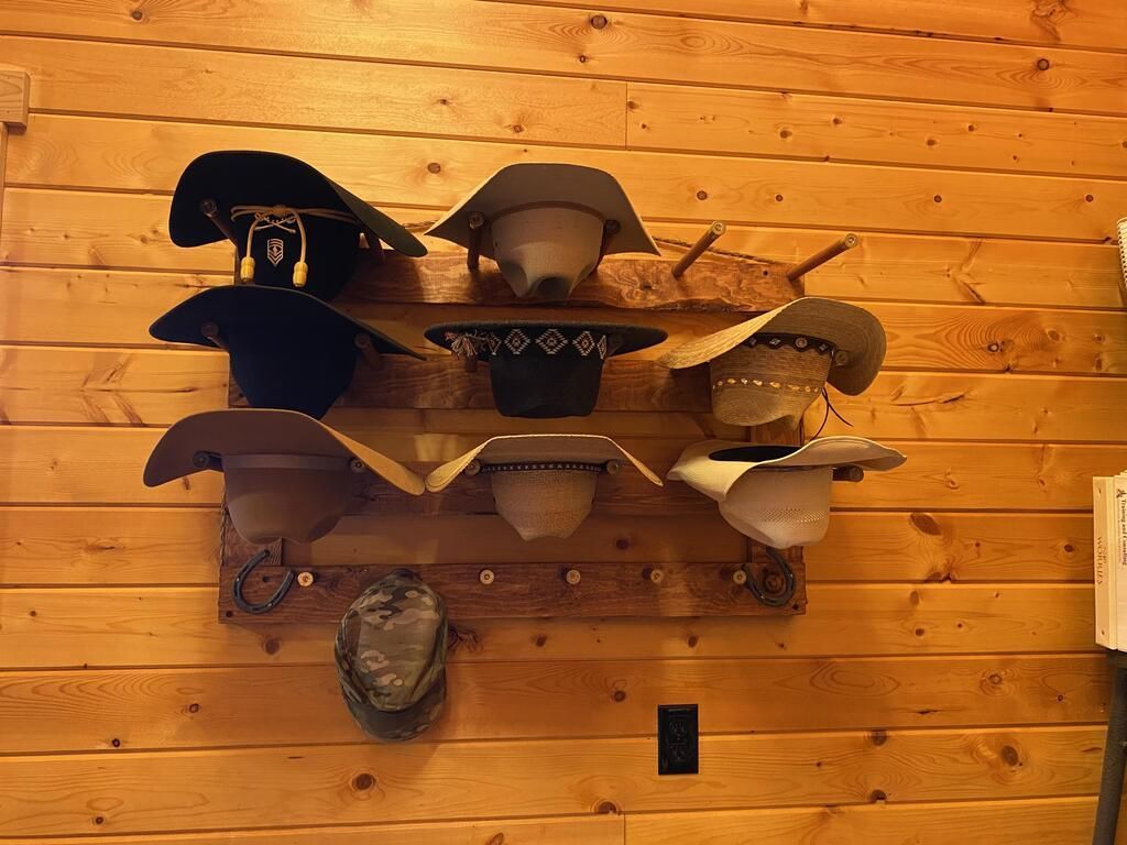 Cowboy hats on a wooden rack mounted on a wood paneled wall.