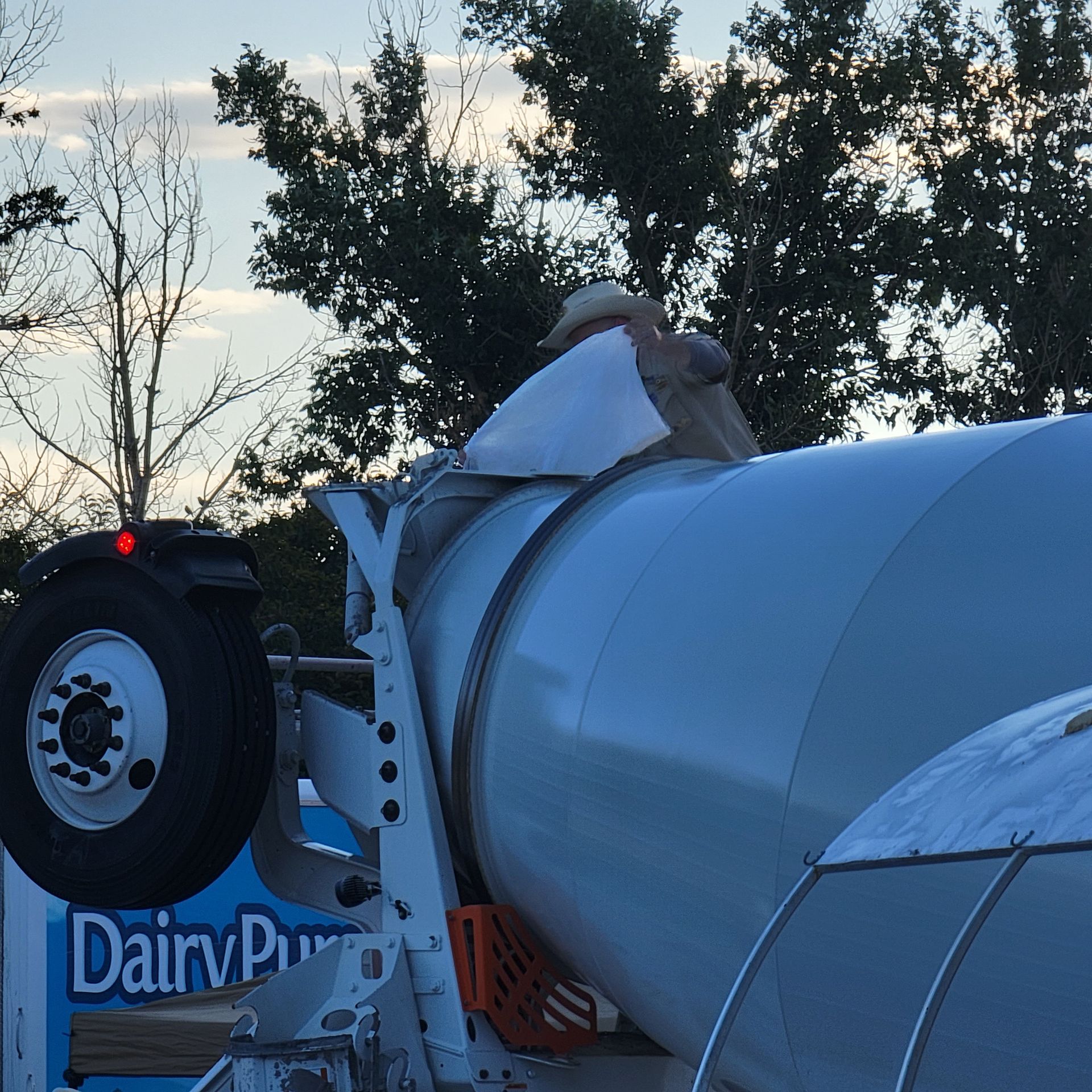 Cement truck with a large, white drum against a blue sky, trees in the background.