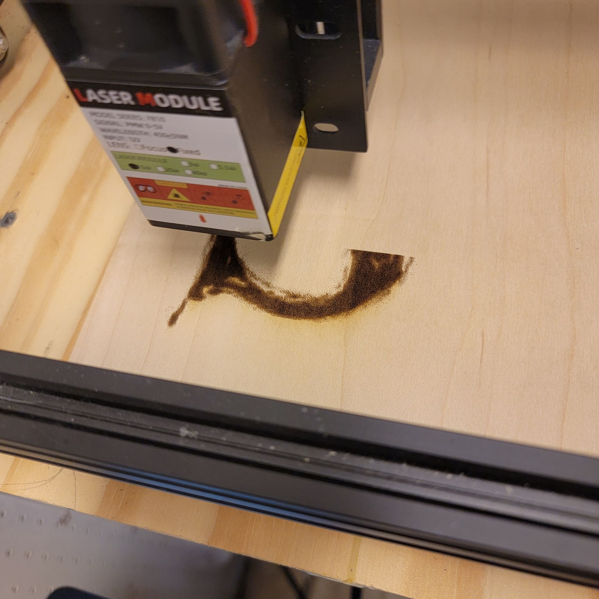 Laser engraver burning wood in a workshop setting, with smoke and scorch marks.