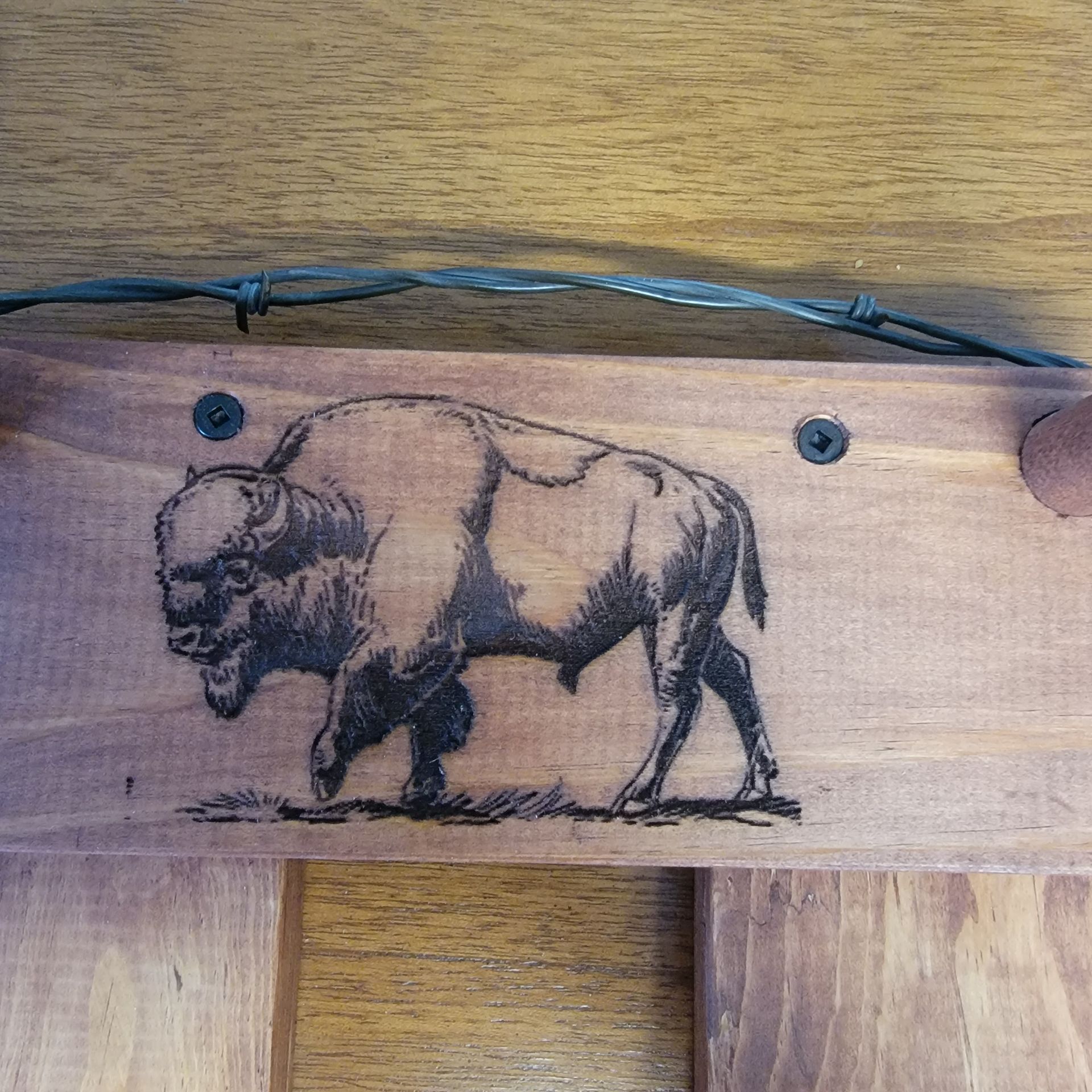Wooden sign with etched bison; barbed wire and screws visible.