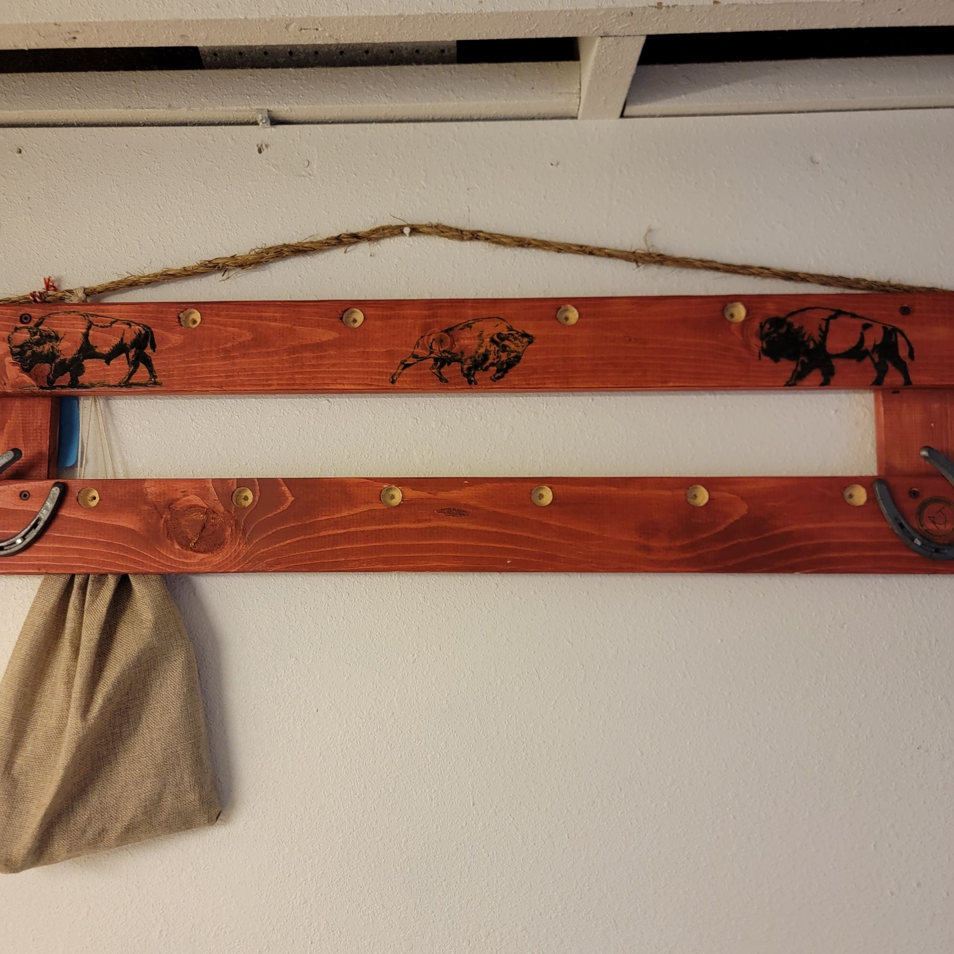Wooden coat rack with bison silhouettes and horseshoe hooks, stained red and hung with twine.