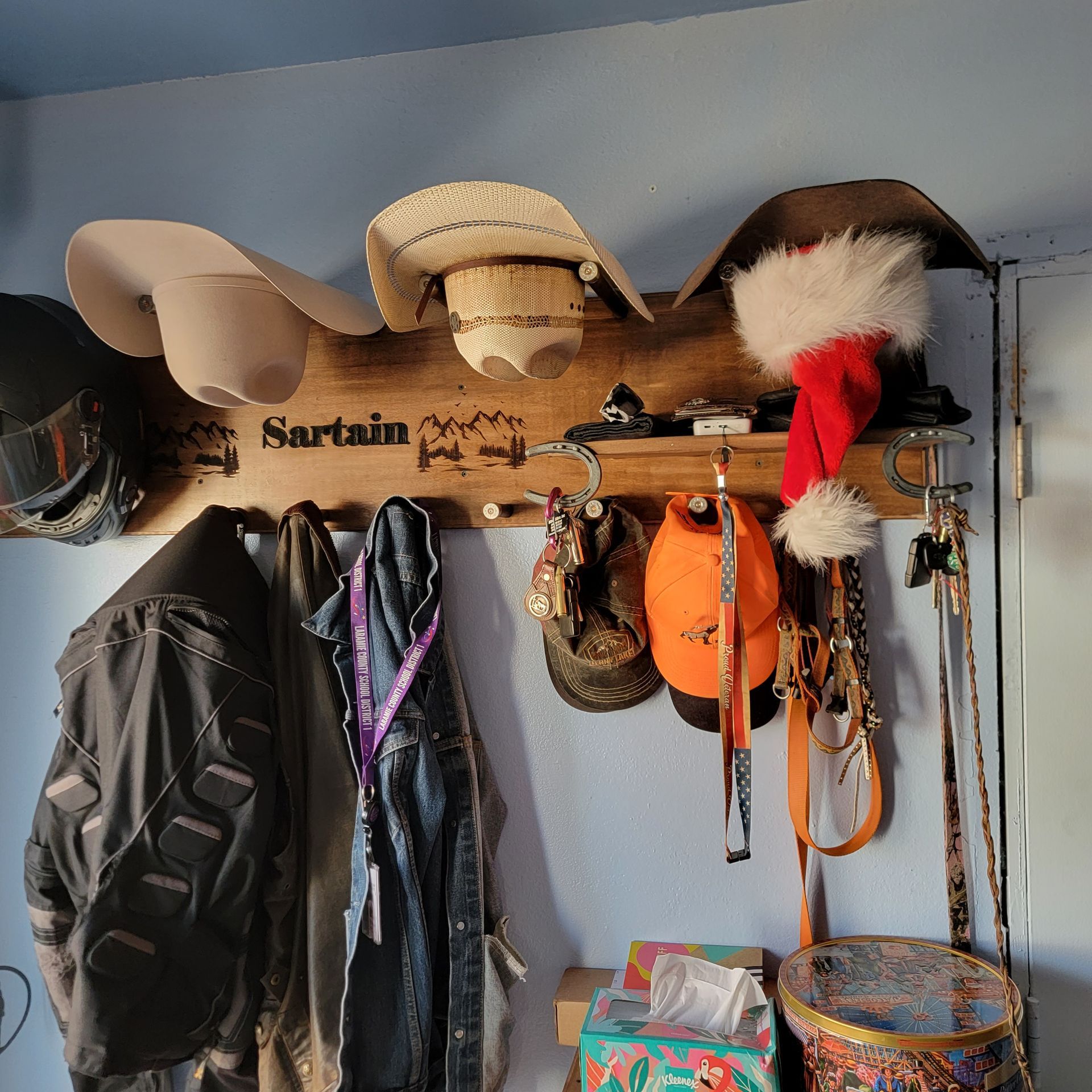 A wooden hat rack with hats and coats hanging, including a Santa hat.