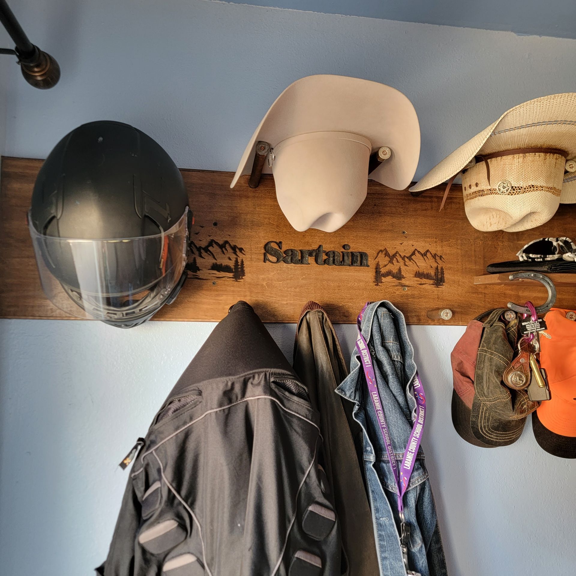 Wooden wall-mounted rack holding a helmet, hats, and coats. Text reads 
