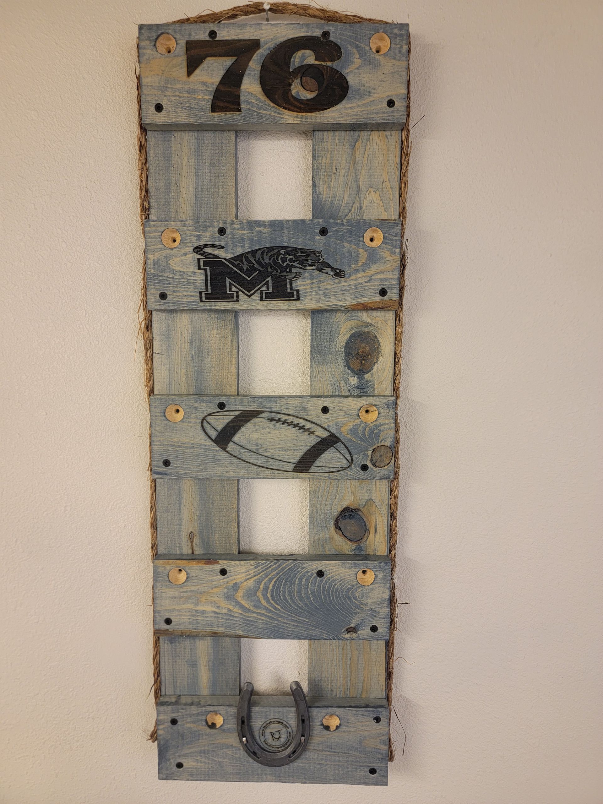 Wooden sign with the number 76, a football, a horseshoe, and a symbol on blue planks.