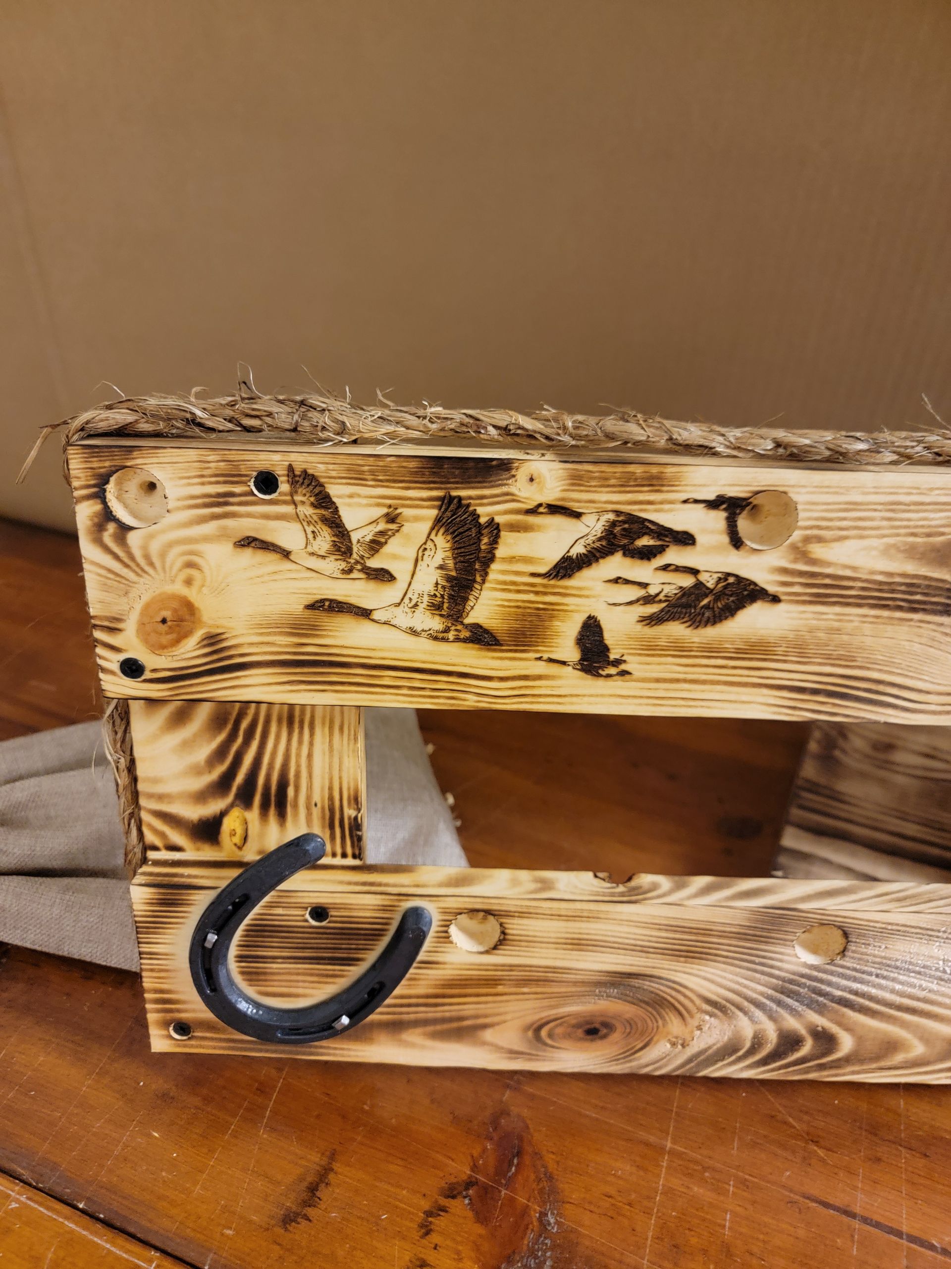 Wooden pallet shelf with burnt design, a horseshoe hook, and straw trim.