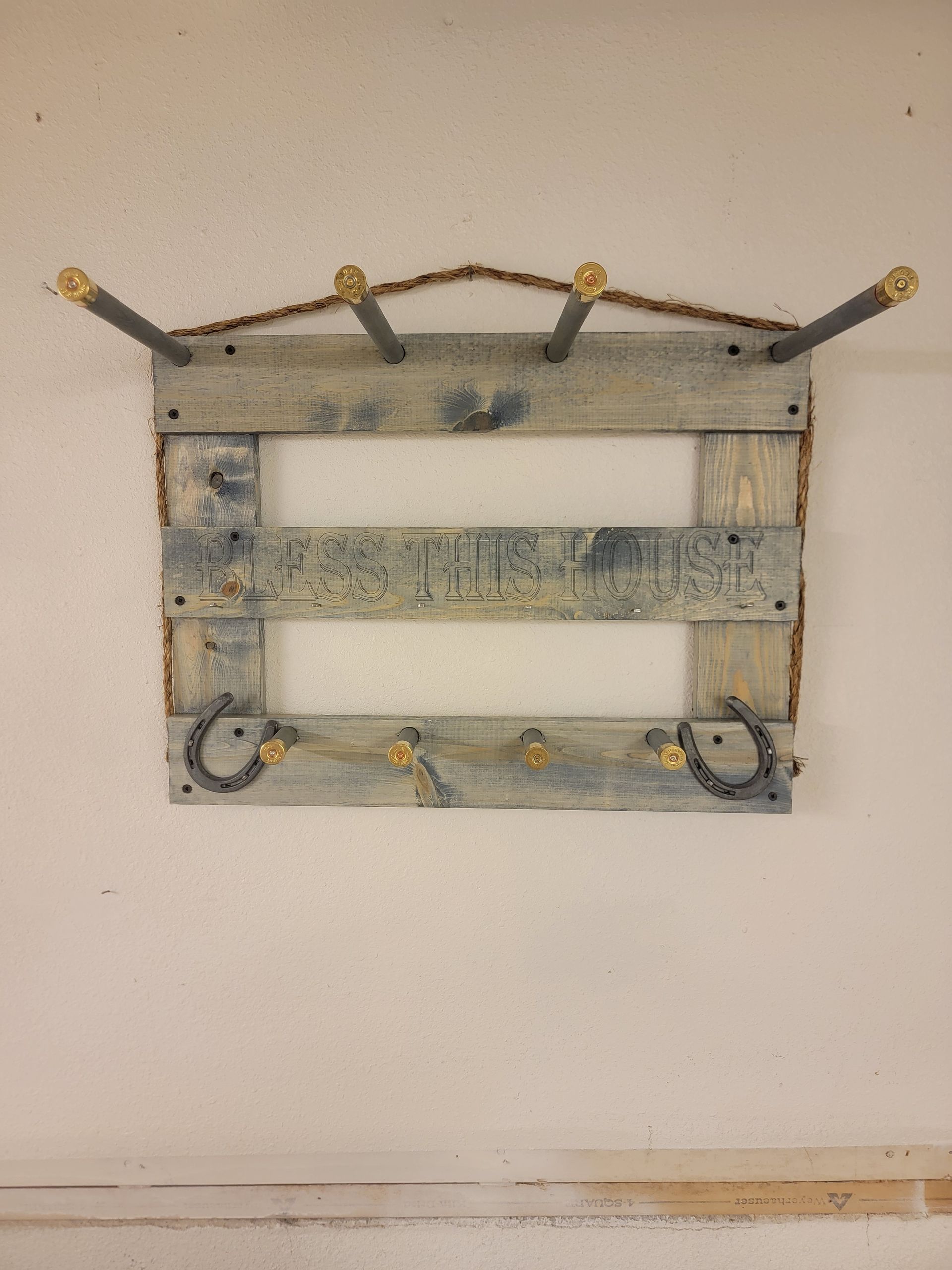 Wooden coat rack made of pallet wood, with metal hooks and horseshoe accents, mounted on a white wall.