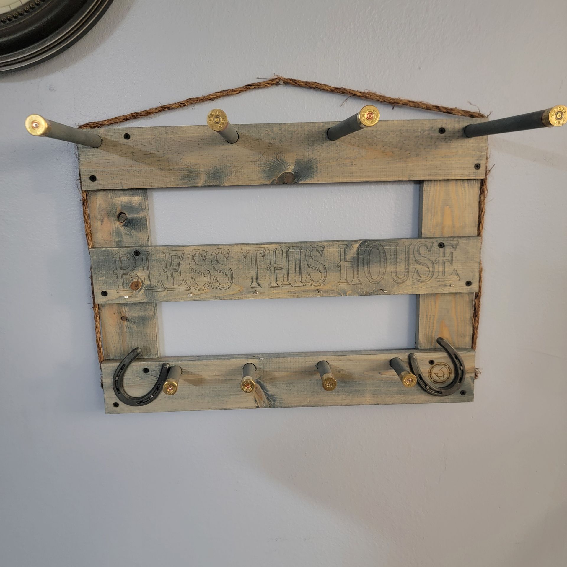 Rustic wooden wall-mounted rack with hooks made from bullet casings and horseshoes.