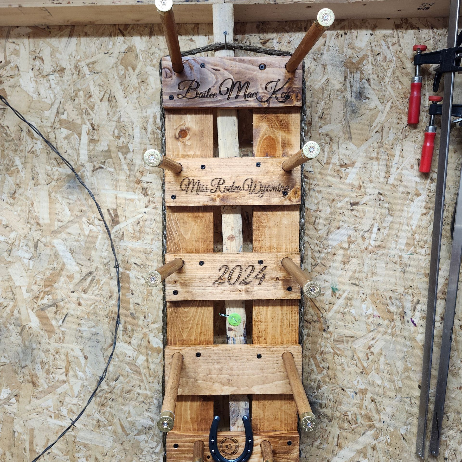 Wooden horseshoe game board with pegs, horseshoe, and the year 2024. Mounted on a wood panel wall.