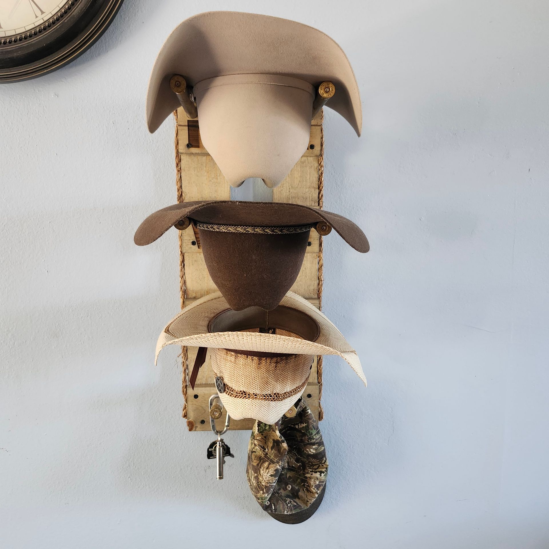 Three cowboy hats on a wall-mounted rack. Hats are tan, brown, and white. A key holder is at the bottom.