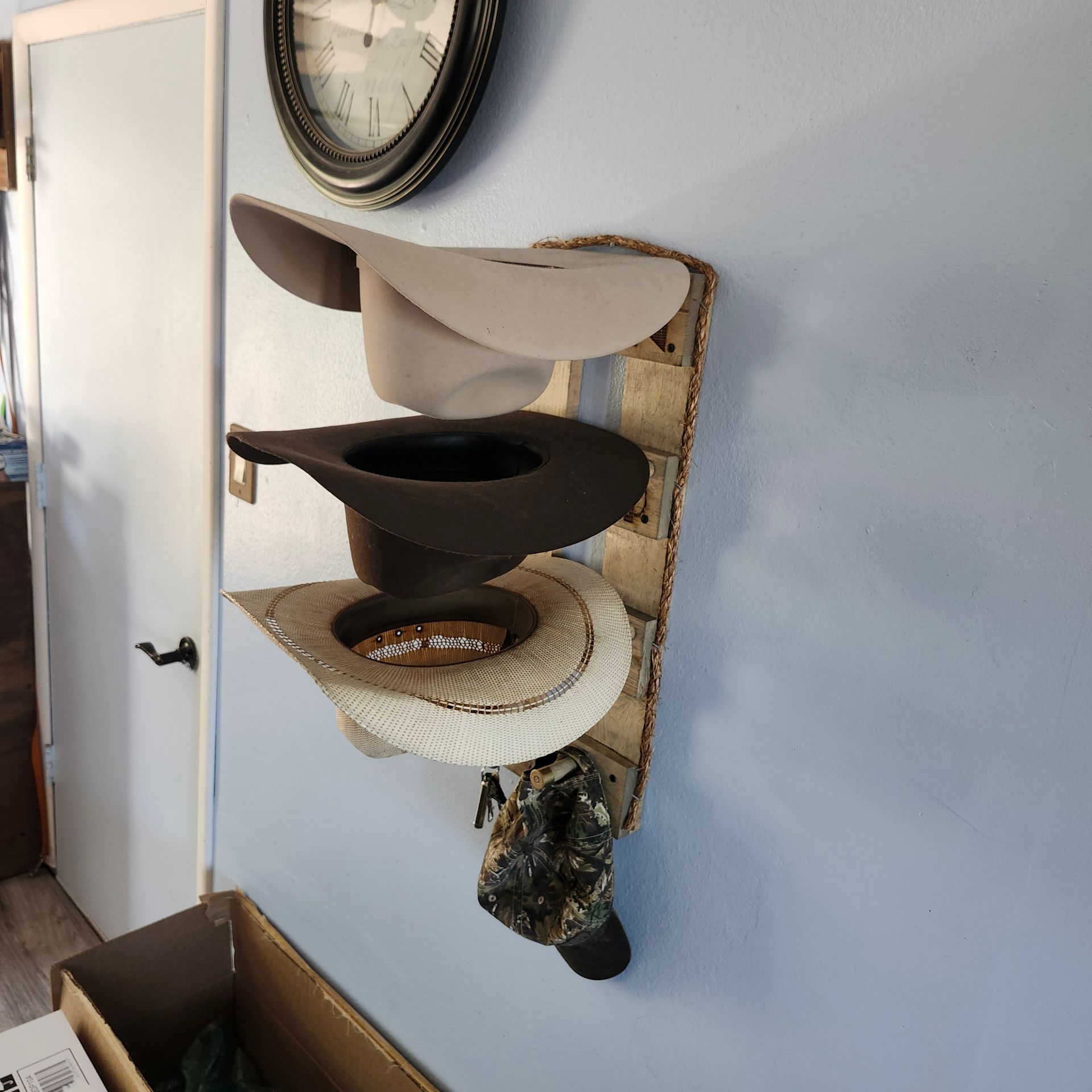 Cowboy hats displayed on a rustic, wall-mounted hat rack, with a clock in the background.