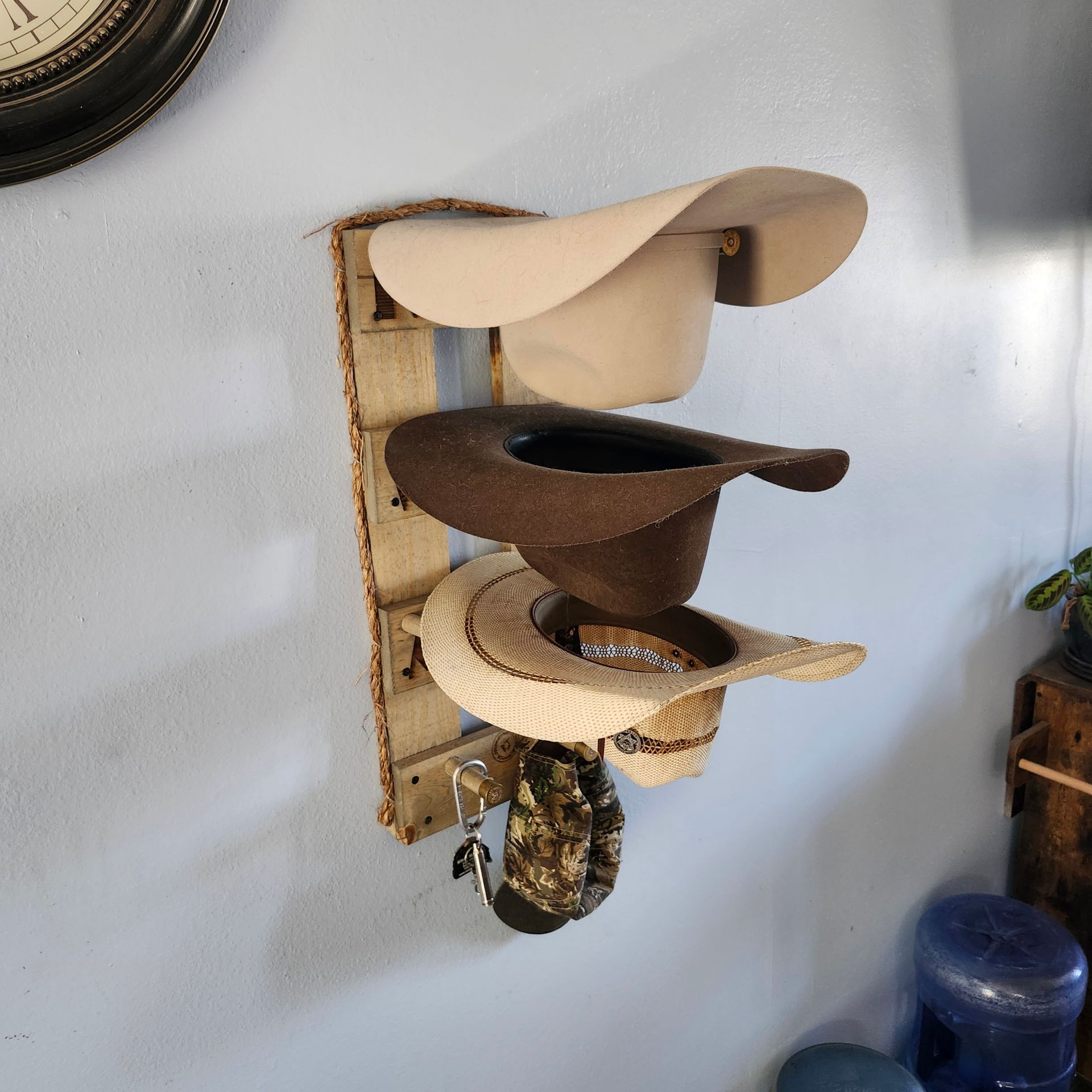 A wall-mounted hat rack with three hats of different colors hanging on it.