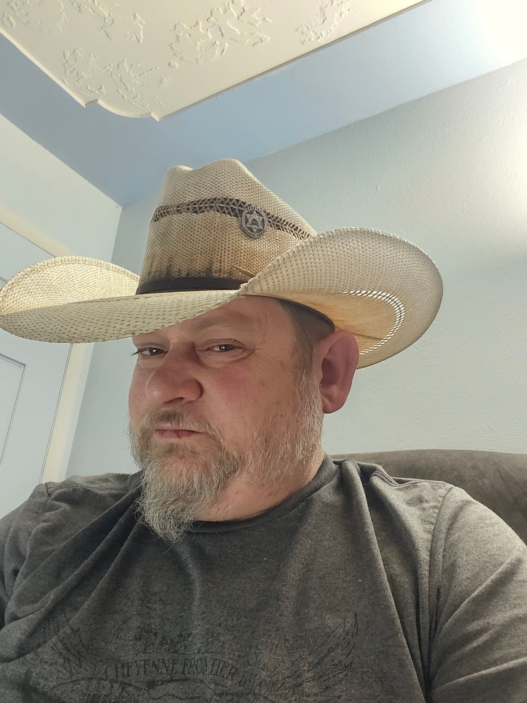 Man with a straw cowboy hat, serious expression, wearing a gray shirt indoors.