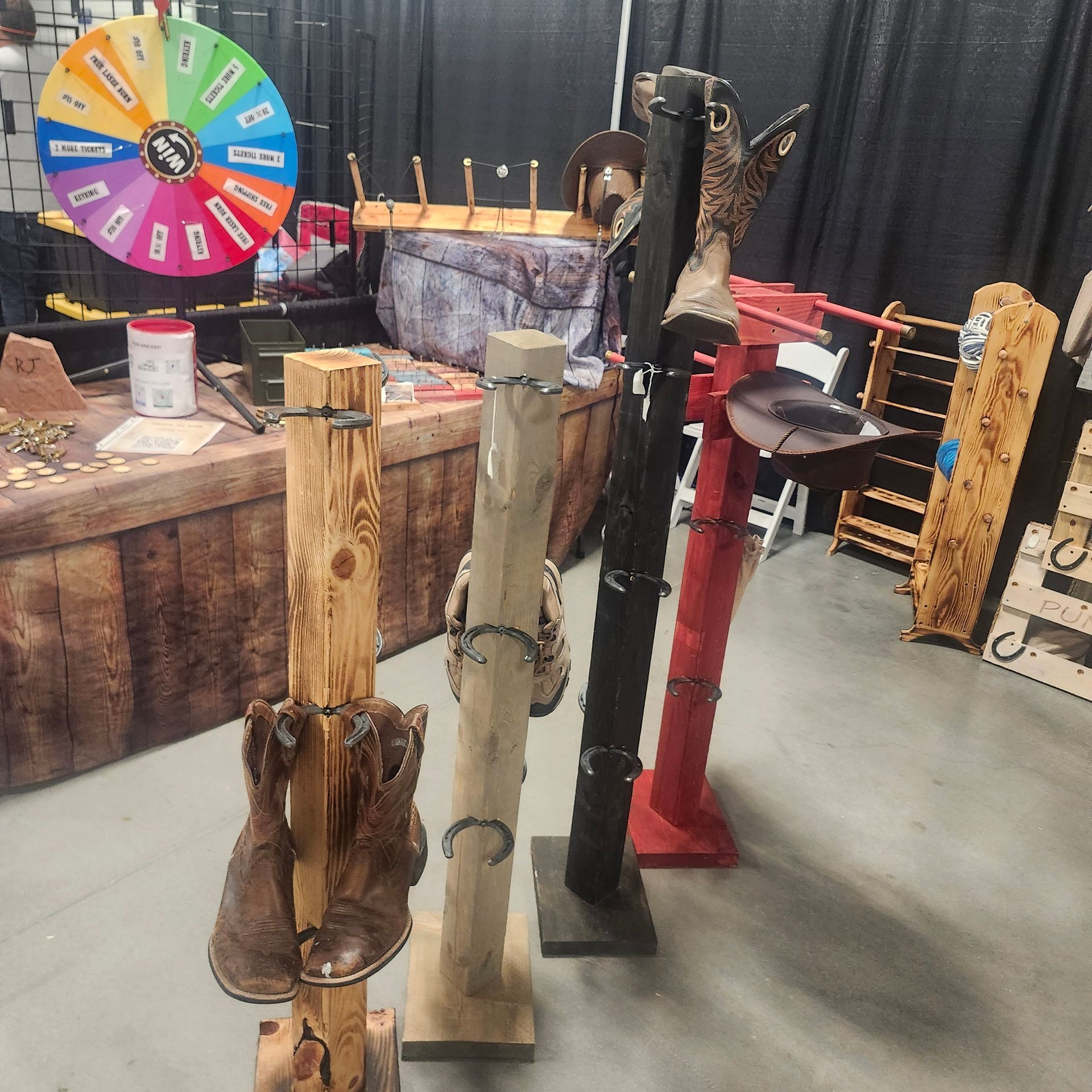 Boots displayed on wooden stands at a market, with a prize wheel in the background.