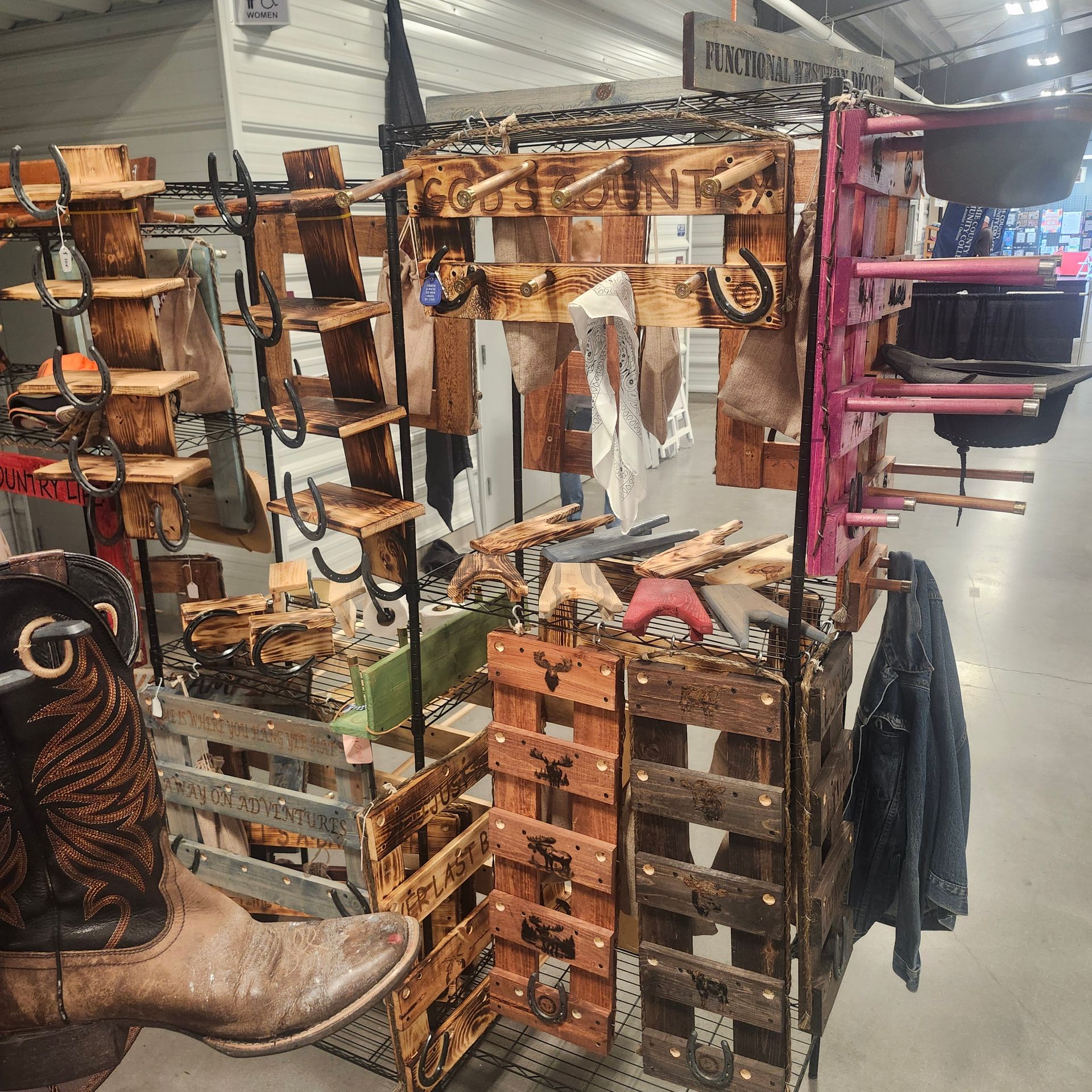 Booth display of wooden crafts and cowboy boots at a market.