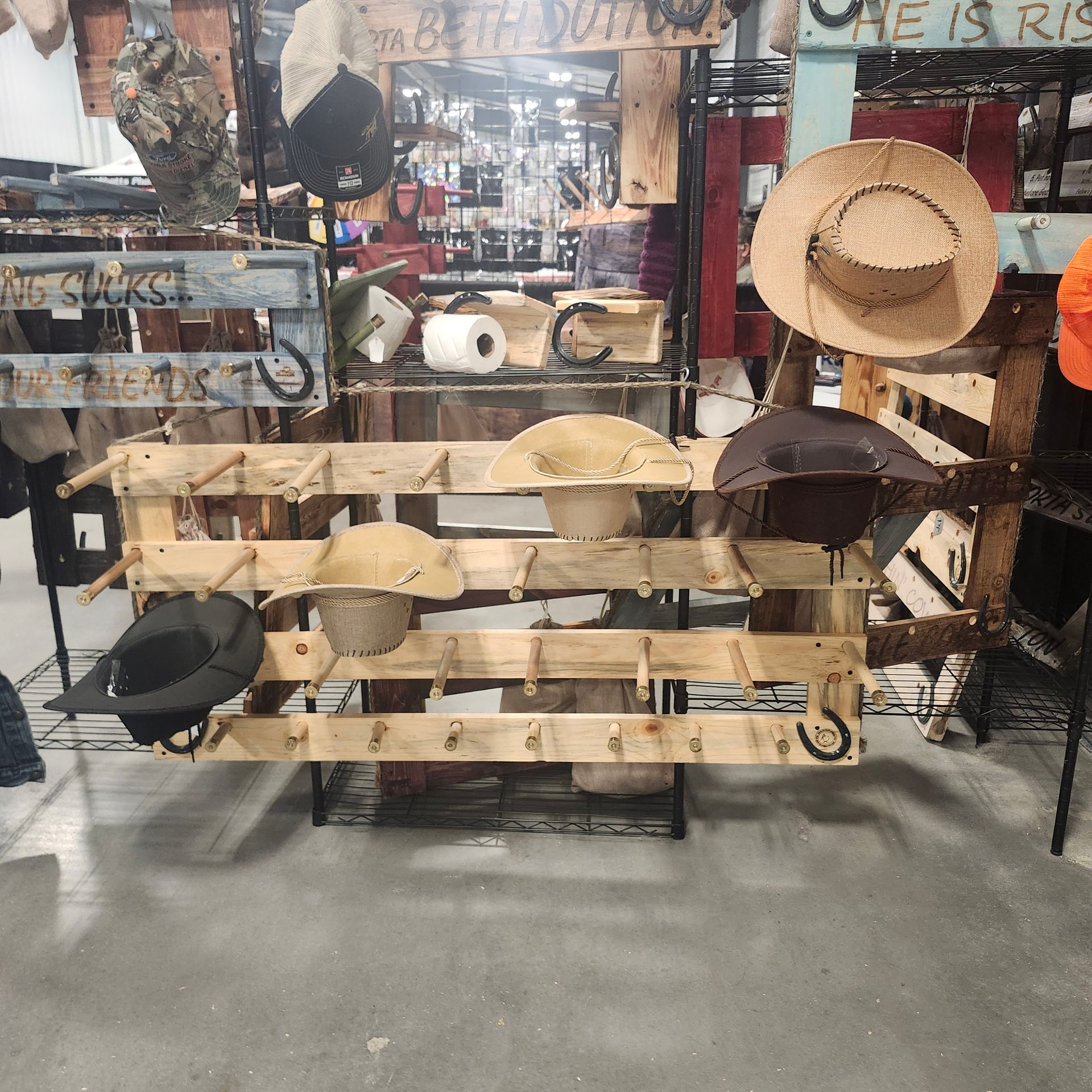 Hats displayed on a wooden rack, set in a store. Some hats are straw, some cloth, and some are camo.