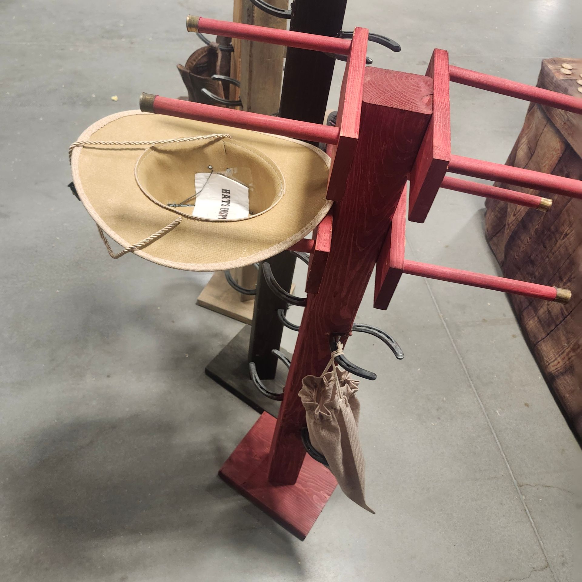 Red wooden hat rack with a tan hat and bag hanging, standing on a gray floor.