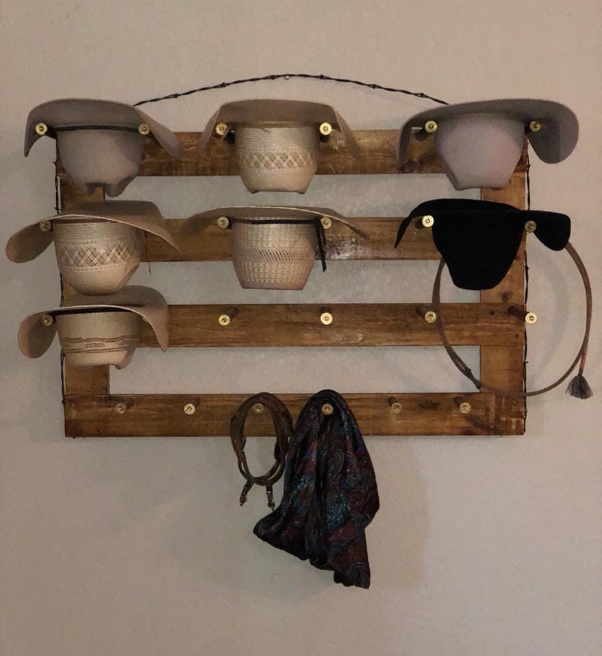 Wooden hat rack with six cowboy hats, a rope, and a scarf on a wall.