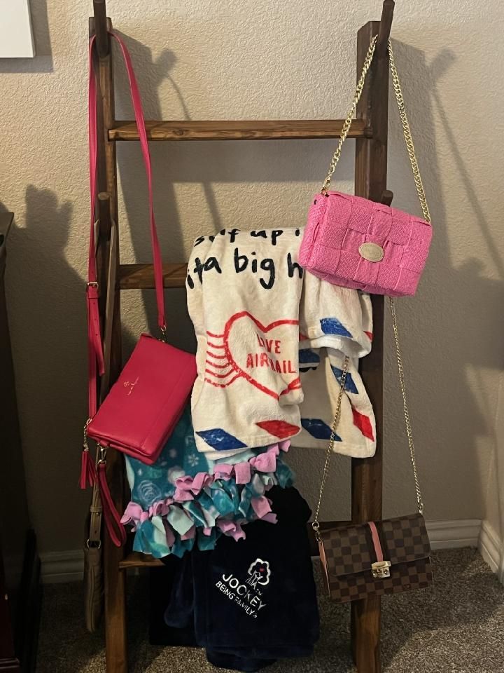 Wooden ladder with handbags and a towel draped over the rungs; pink, brown, and blue colors.