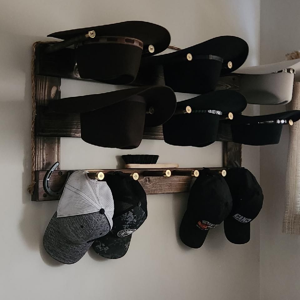 A wooden hat rack on a wall displaying various hats. Some hats are on shelves, others hang on hooks.