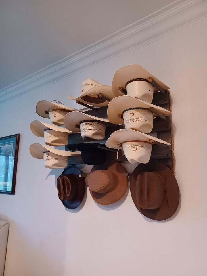 Cowboy hats displayed on a rustic wooden wall-mounted rack. Hats are various colors, shapes. Wall is white.