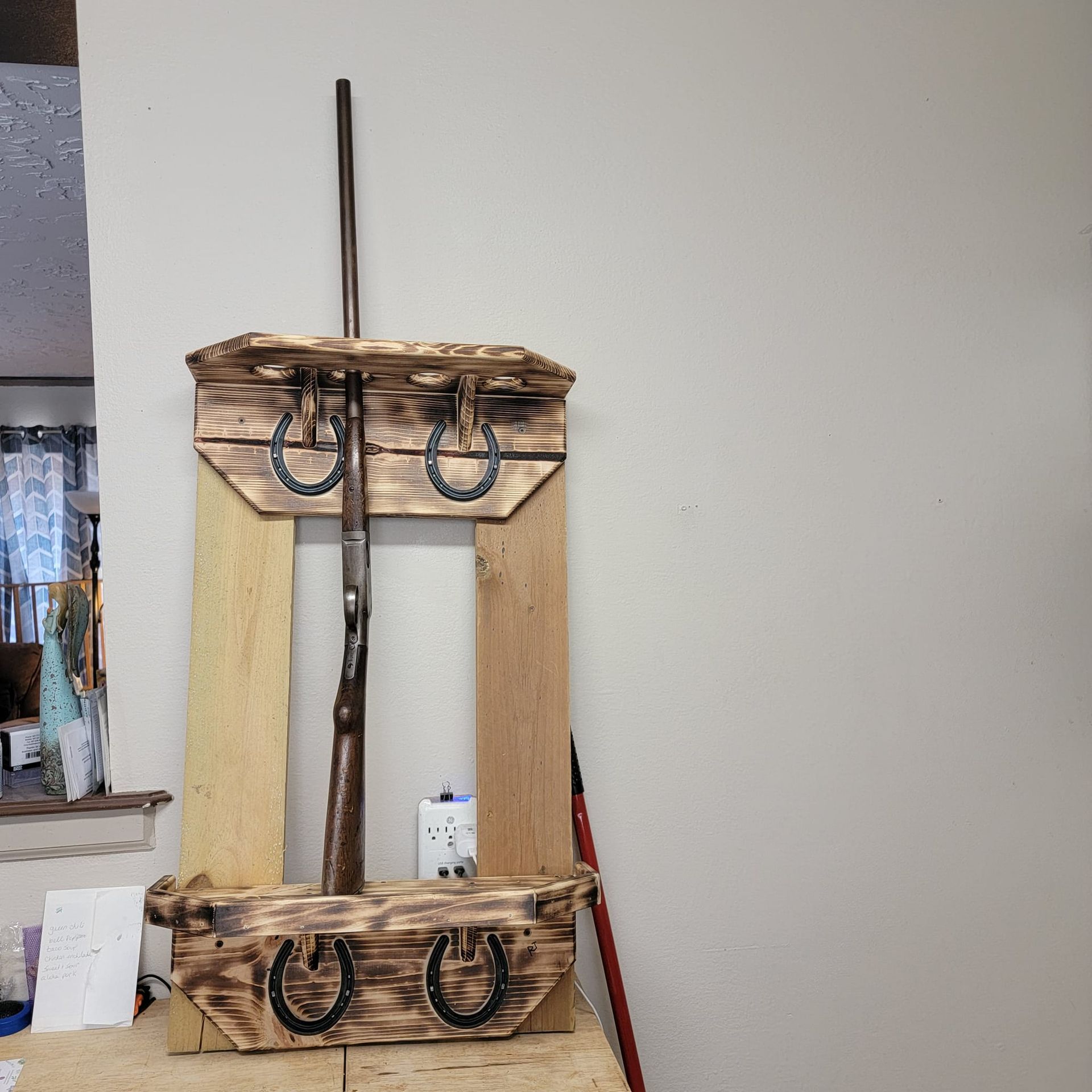 Wooden gun rack with a rifle inside, decorated with horseshoes.