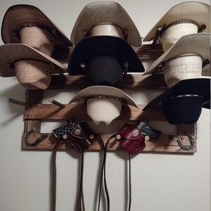 Cowboy hats displayed on a wooden rack, some with leather pouches and straps hanging below.