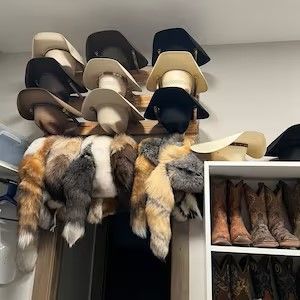 Cowboy hats on a rack above animal fur and boots in a closet.