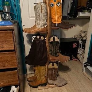 Wooden boot rack with several pairs of cowboy boots, in various colors and designs.