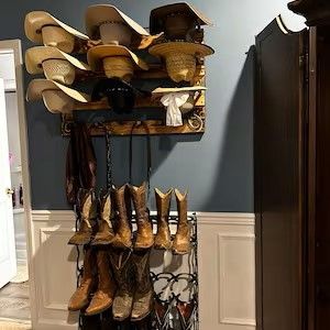 Wall-mounted cowboy hat rack with hats and boot rack holding boots against blue wall.