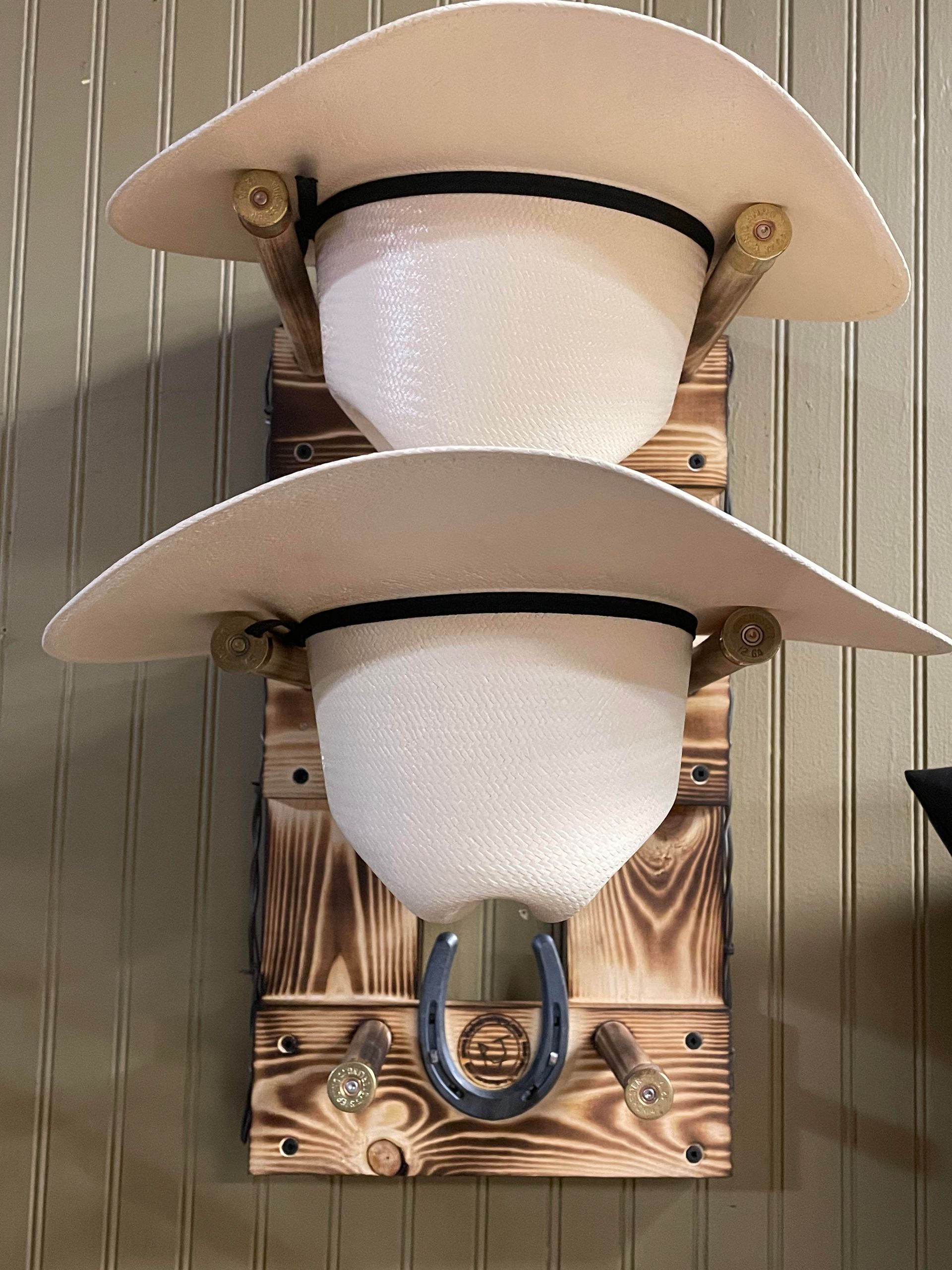 Two cowboy hats on a wooden rack with horseshoe and decorative wood burning.