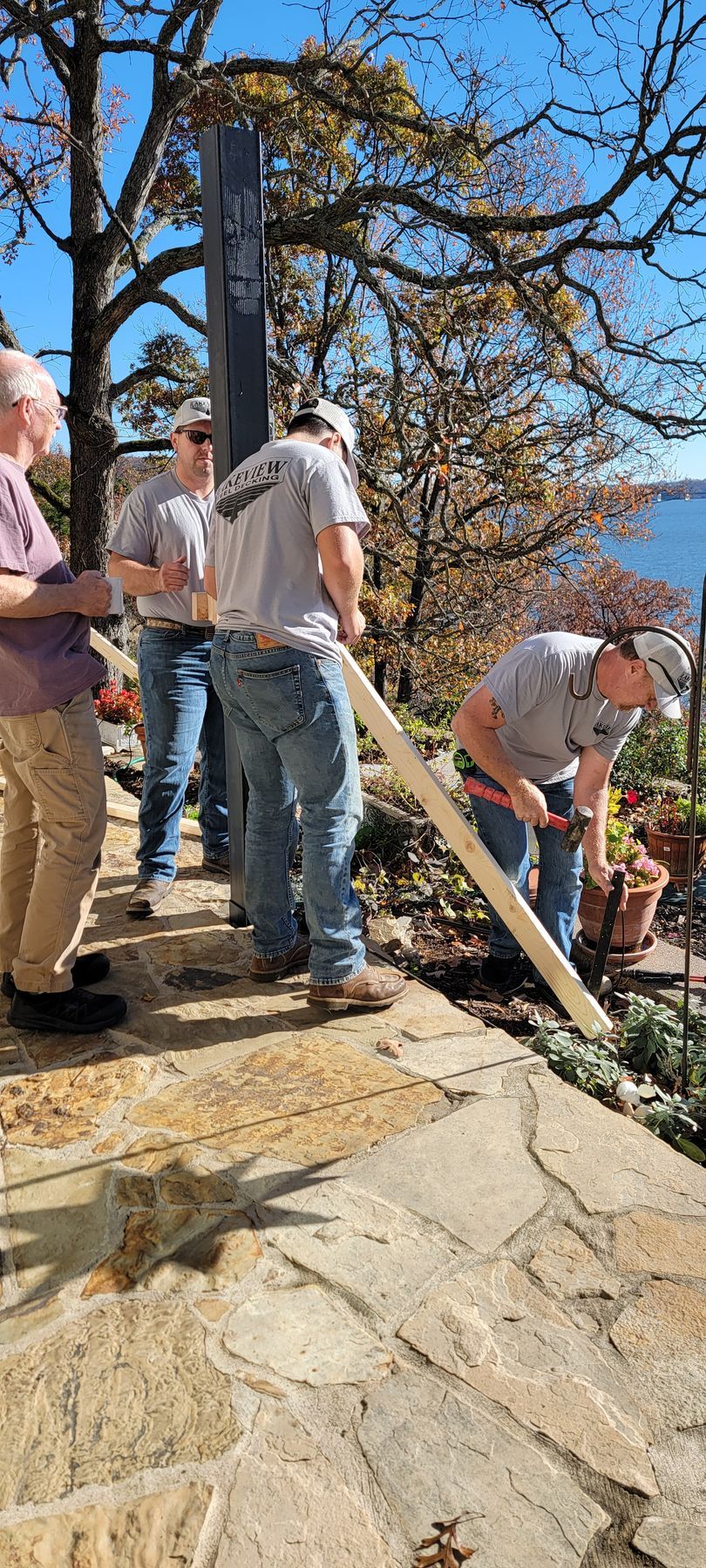 Workers repairing a stone walkway on a hillside with trees and a clear blue sky.