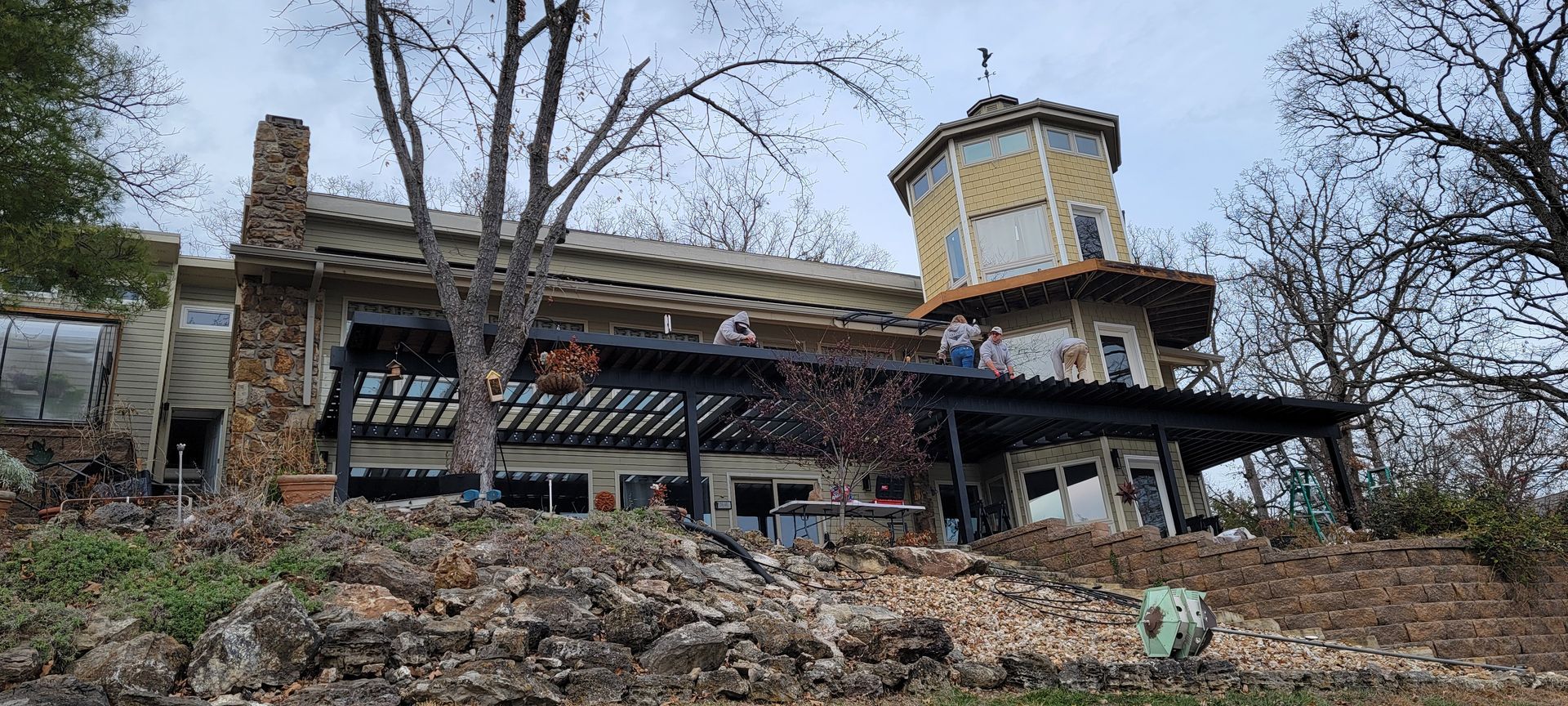 Abandoned house on a wooded hillside, with a deck and round tower under bare winter trees.