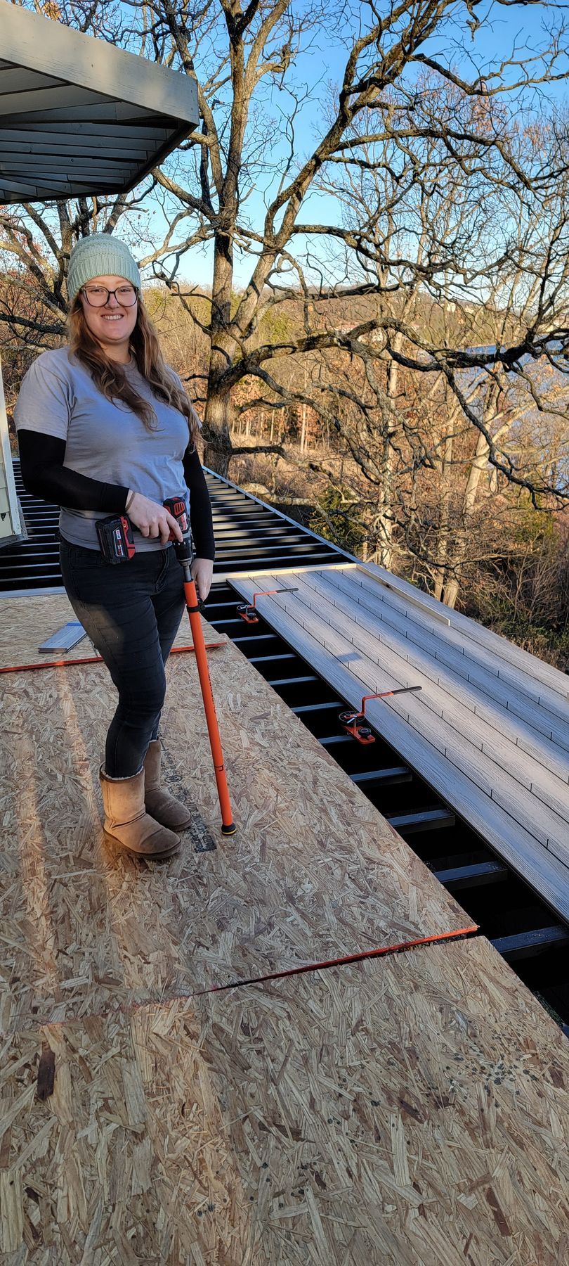 Woman standing on a rooftop deck holding an orange leash, with trees in the background.