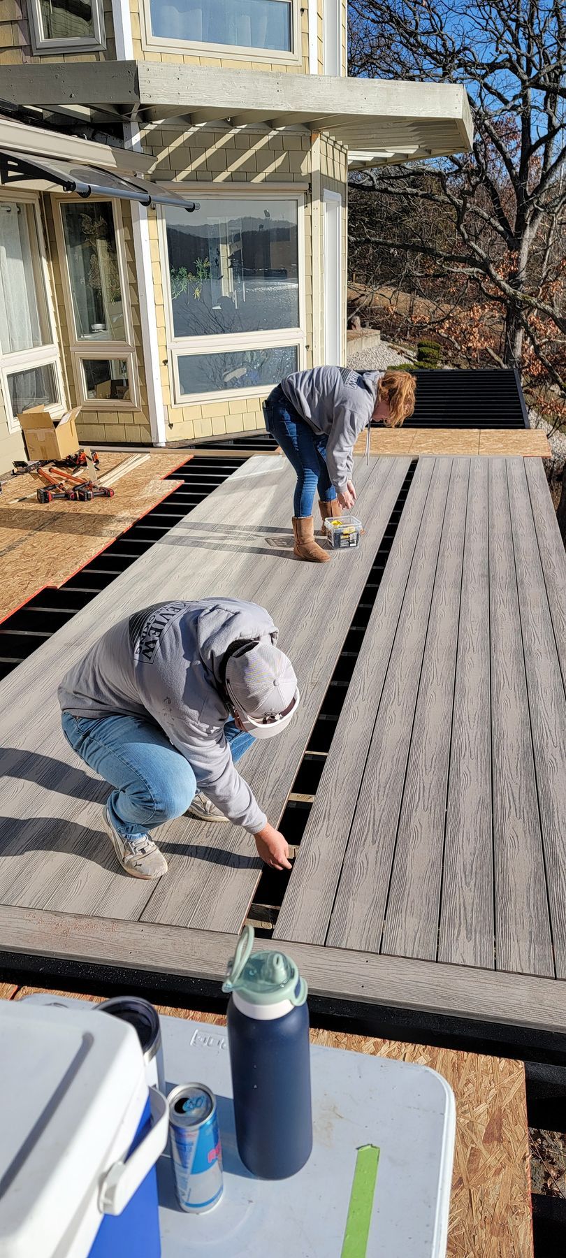 Two workers staining a wooden deck outside a house on a sunny day